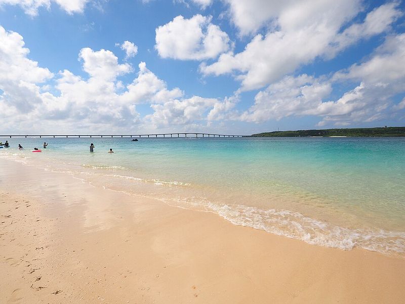 宮古ブルーの遠浅の海と白い砂浜で泳ぐ人々・遠くに架かる橋