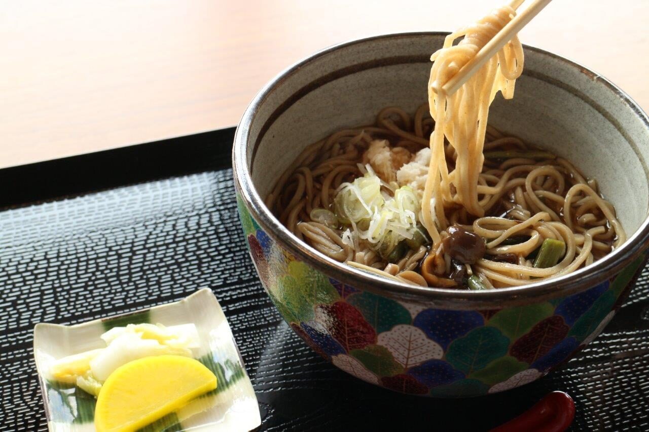 箸で持ち上げられた手打ちそばと、おろしや薬味が添えられた様子
