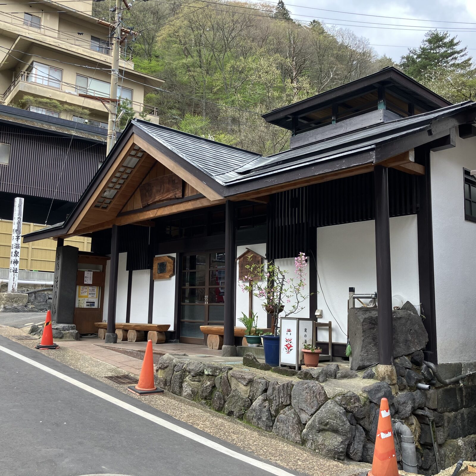 鳴子温泉神社の社号標と、鳥居前に佇む共同浴場「滝の湯」