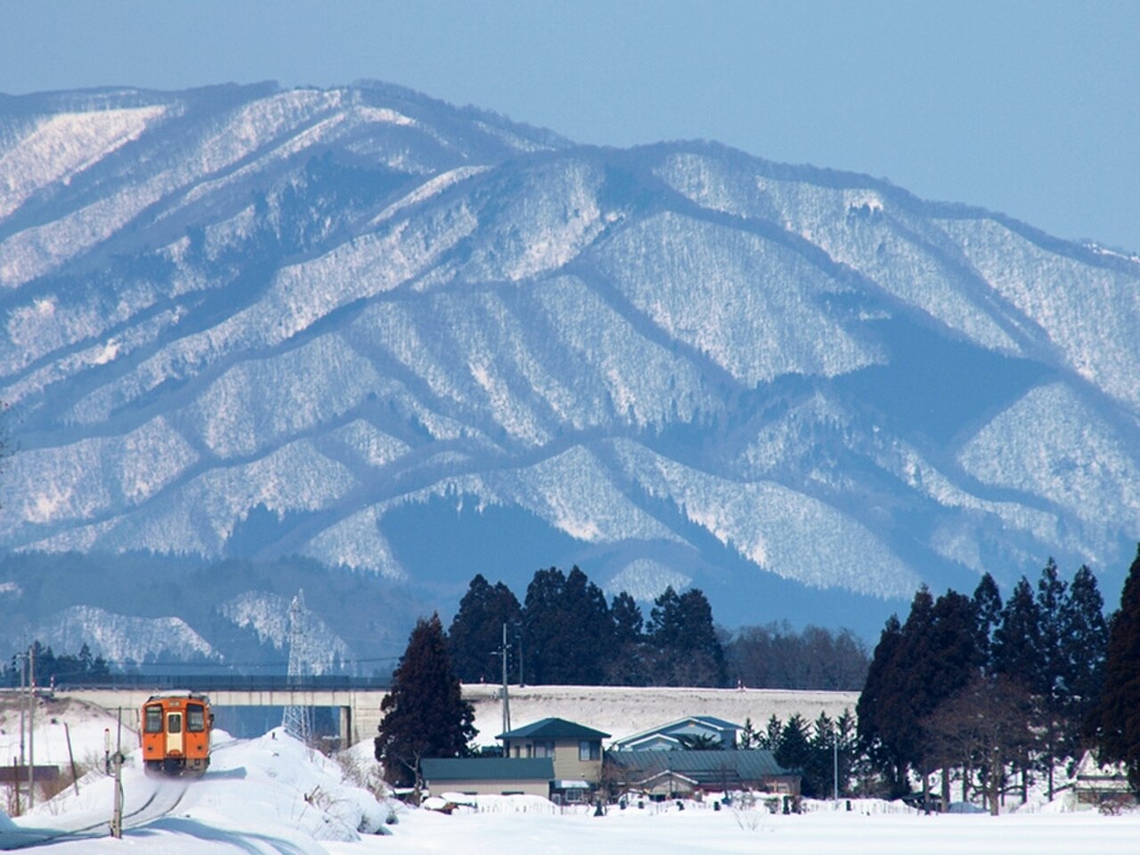 雪山を背景にオレンジ色の列車が雪原を走る冬景色