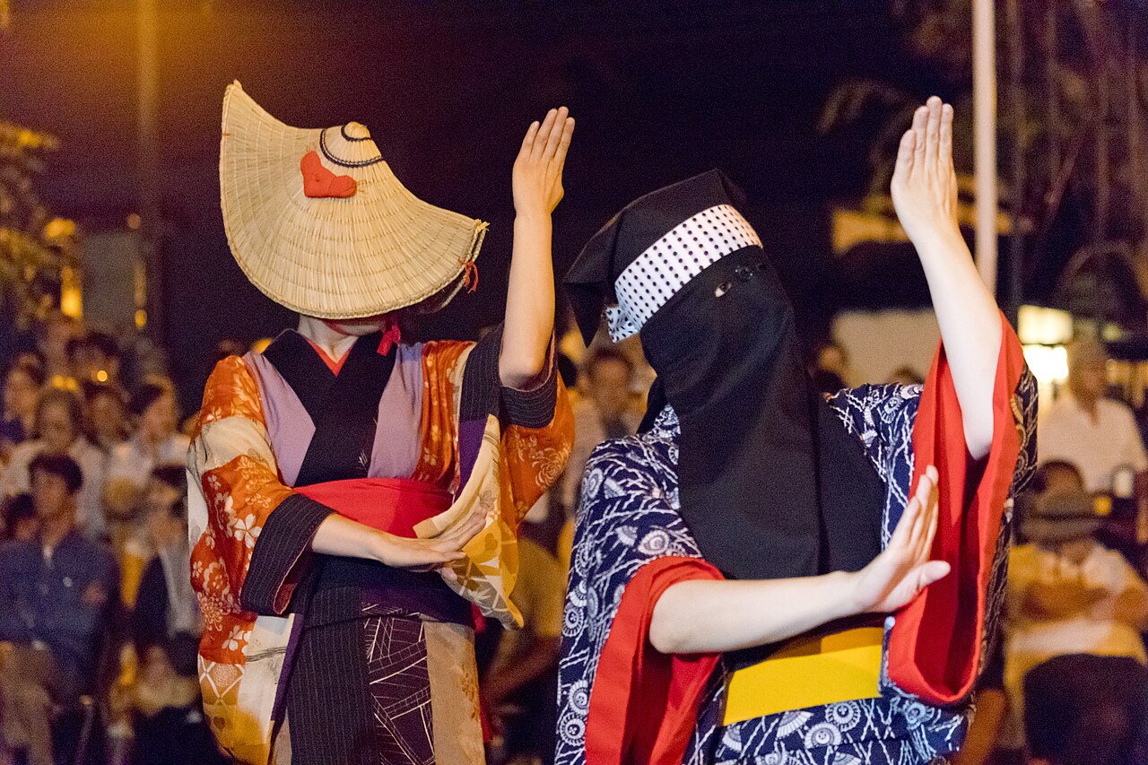 編み笠と黒い彦三頭巾をかぶり両手を挙げて踊る2人の踊り手、夜の会場