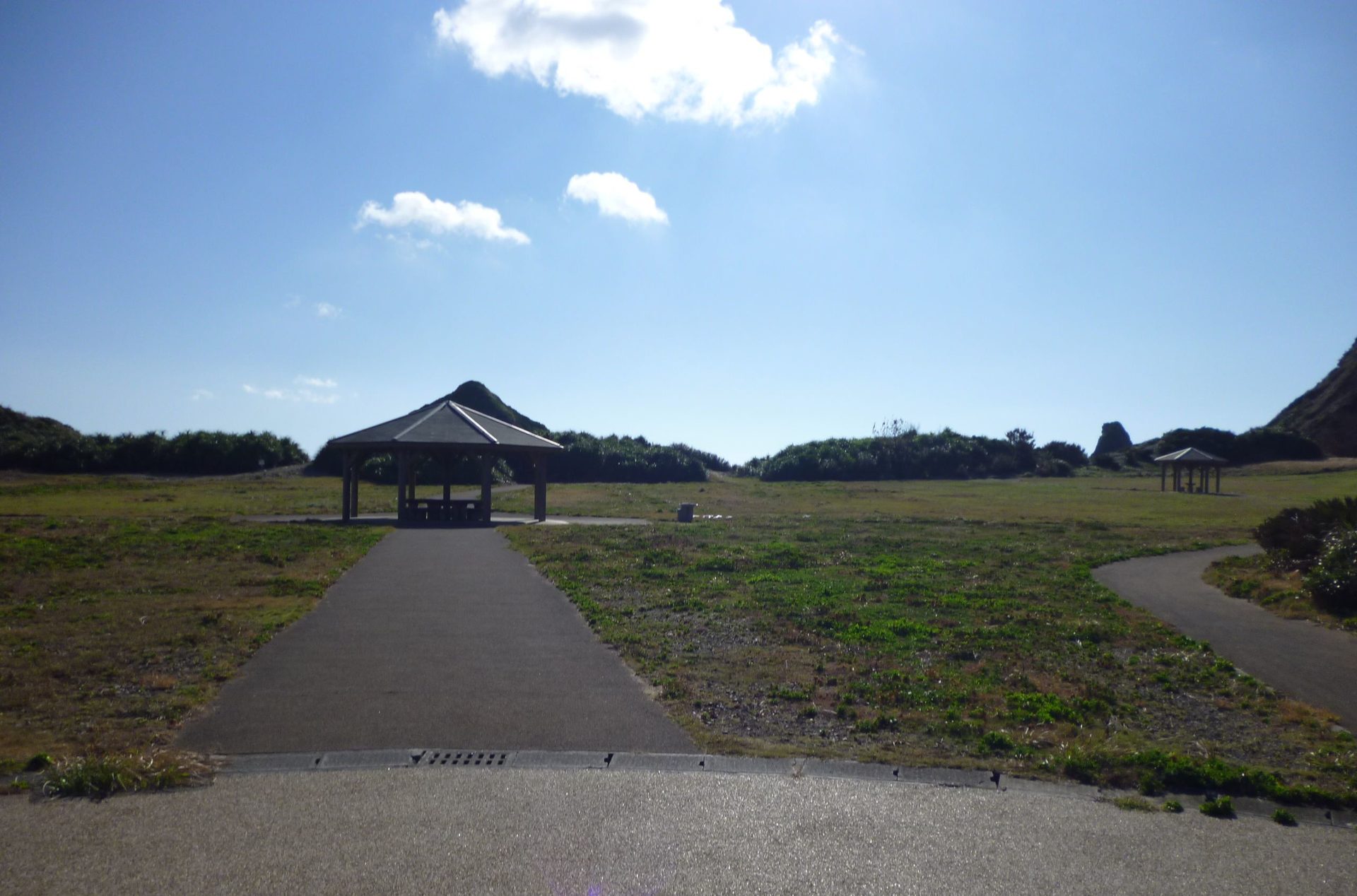 ホノホシ海岸の園地。芝生の中の園路の先に東屋が立つ