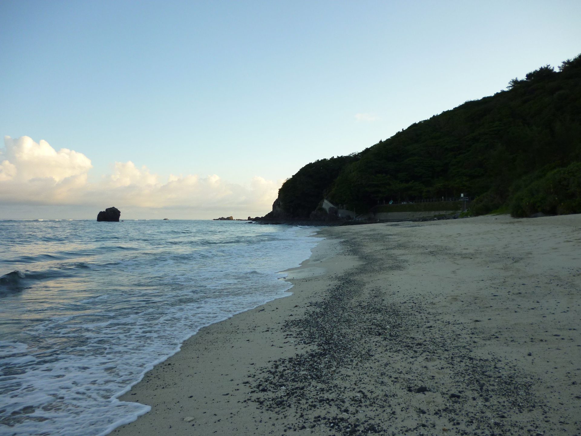 大浜の砂浜と打ち寄せる波。沖に岩が浮かび、右手に緑の岬が迫る