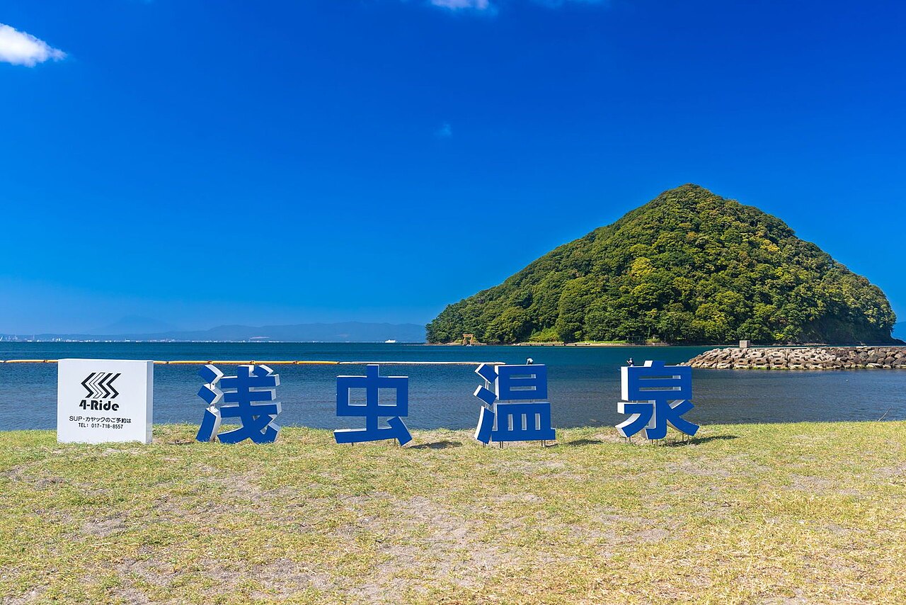 青空の下に立つ「浅虫温泉」の文字モニュメントと、海に浮かぶ湯ノ島