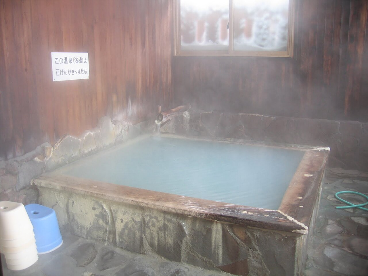 酸ヶ湯温泉の白濁した湯をたたえた湯船と木の湯口