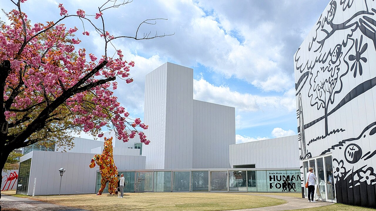 八重桜越しに見る十和田市現代美術館の白い展示棟と花柄の馬のオブジェ