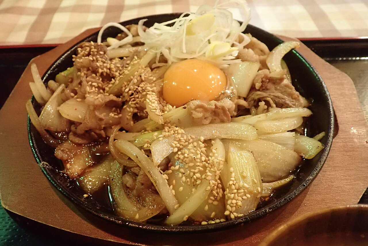 鉄板にのった十和田バラ焼き、卵黄と白髪ねぎ、白ごまがのっている