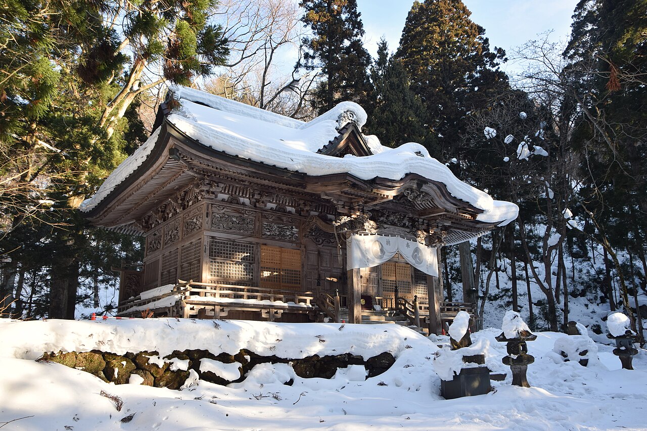 冬の斜光を受ける十和田神社の拝殿と、屋根に厚く積もった雪
