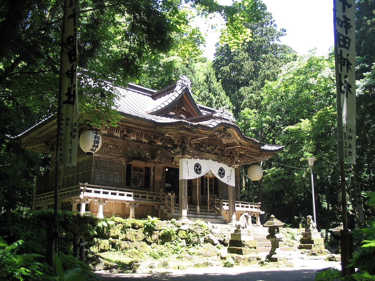新緑に包まれた十和田神社の拝殿と、両脇に立つ奉納の幟旗
