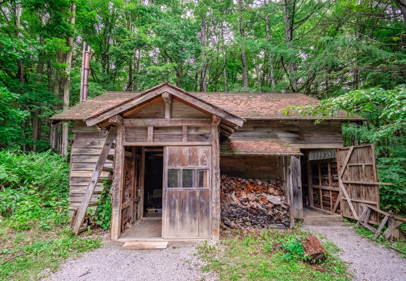 敷地内に残る木造の丸太小屋と積まれた薪