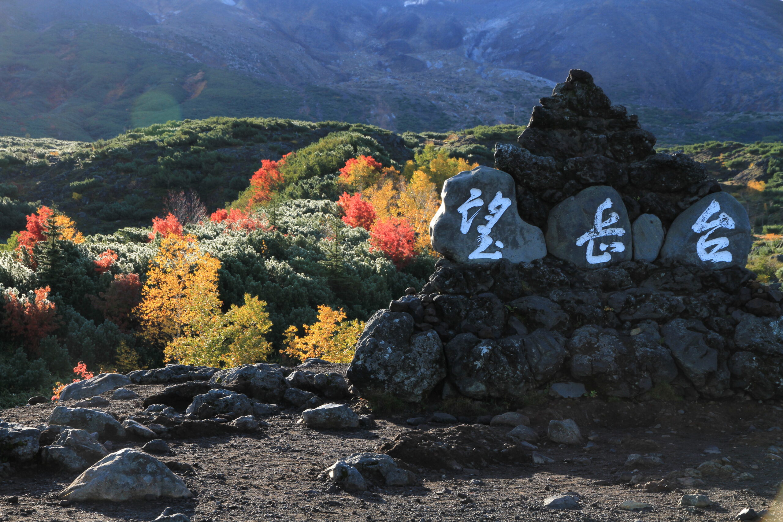 紅葉に彩られた望岳台の石碑と十勝岳の山並み