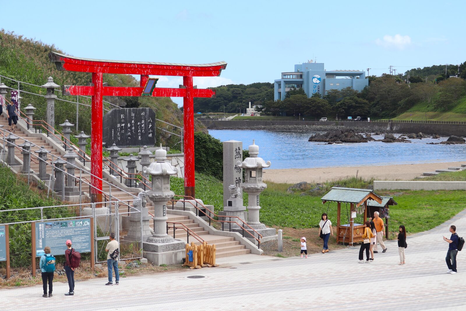蕪嶋神社の鳥居と蕪島海浜公園、背後に八戸市水産科学館マリエント