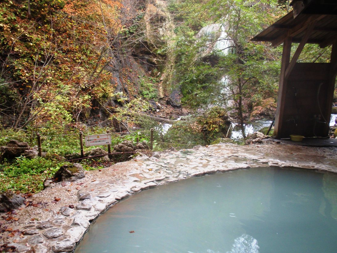白骨温泉の公共野天風呂の乳白色の湯船と渓谷の紅葉