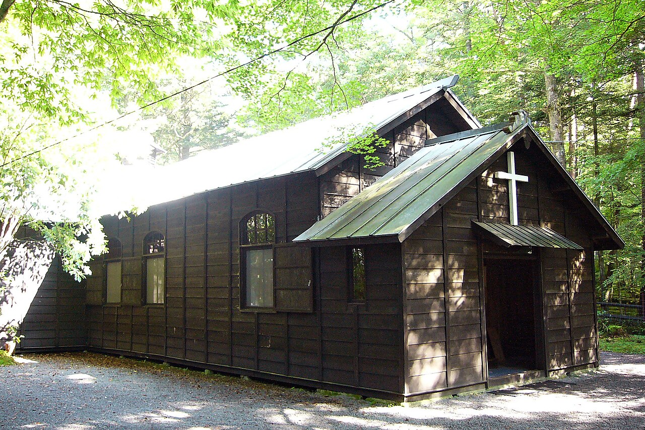 軽井沢ショー記念礼拝堂の側面、緑青色の屋根と焦茶の下見板張り、アーチ窓に落ちる木漏れ日