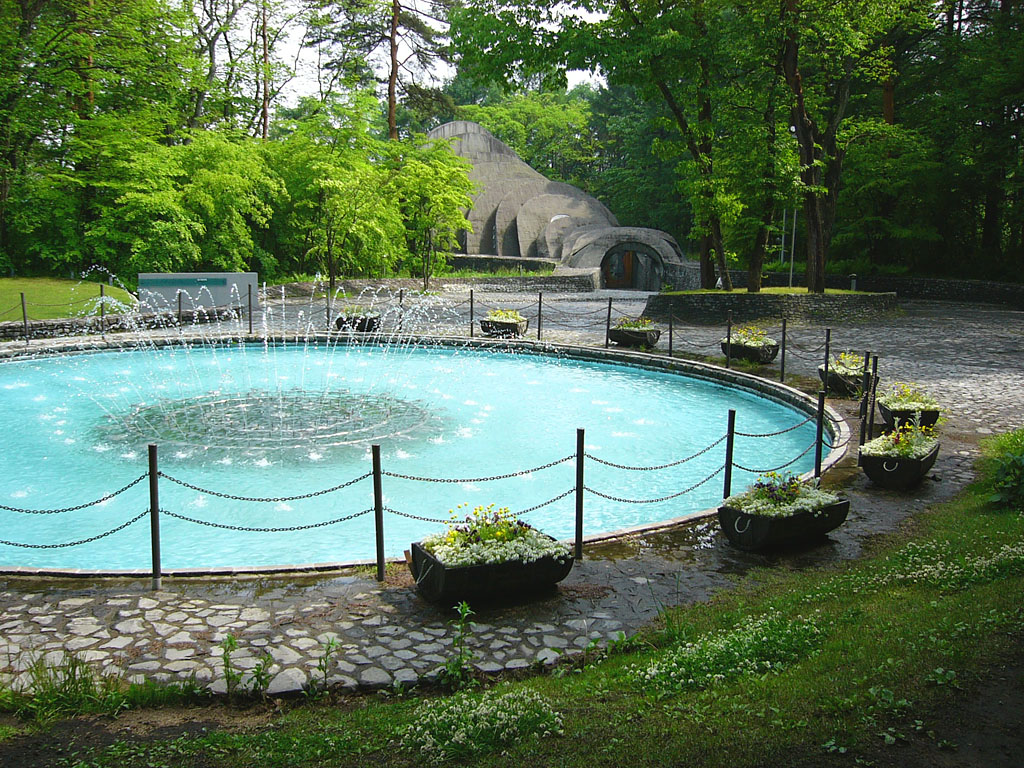 円形の噴水池と花を植えた舟形のプランター、奥に石の教会のアーチ