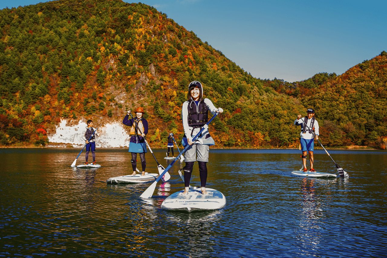 潟沼の湖面でSUPを楽しむ人々と紅葉の外輪山