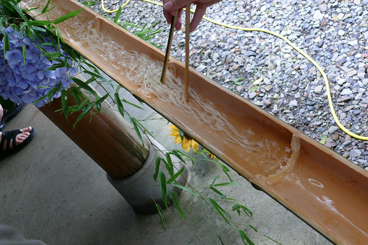 竹の樋を流れるそうめんを箸ですくう様子