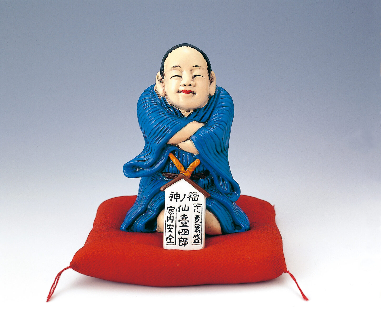 福の神・仙台四郎をかたどった置物、赤い座布団の上に座る姿
