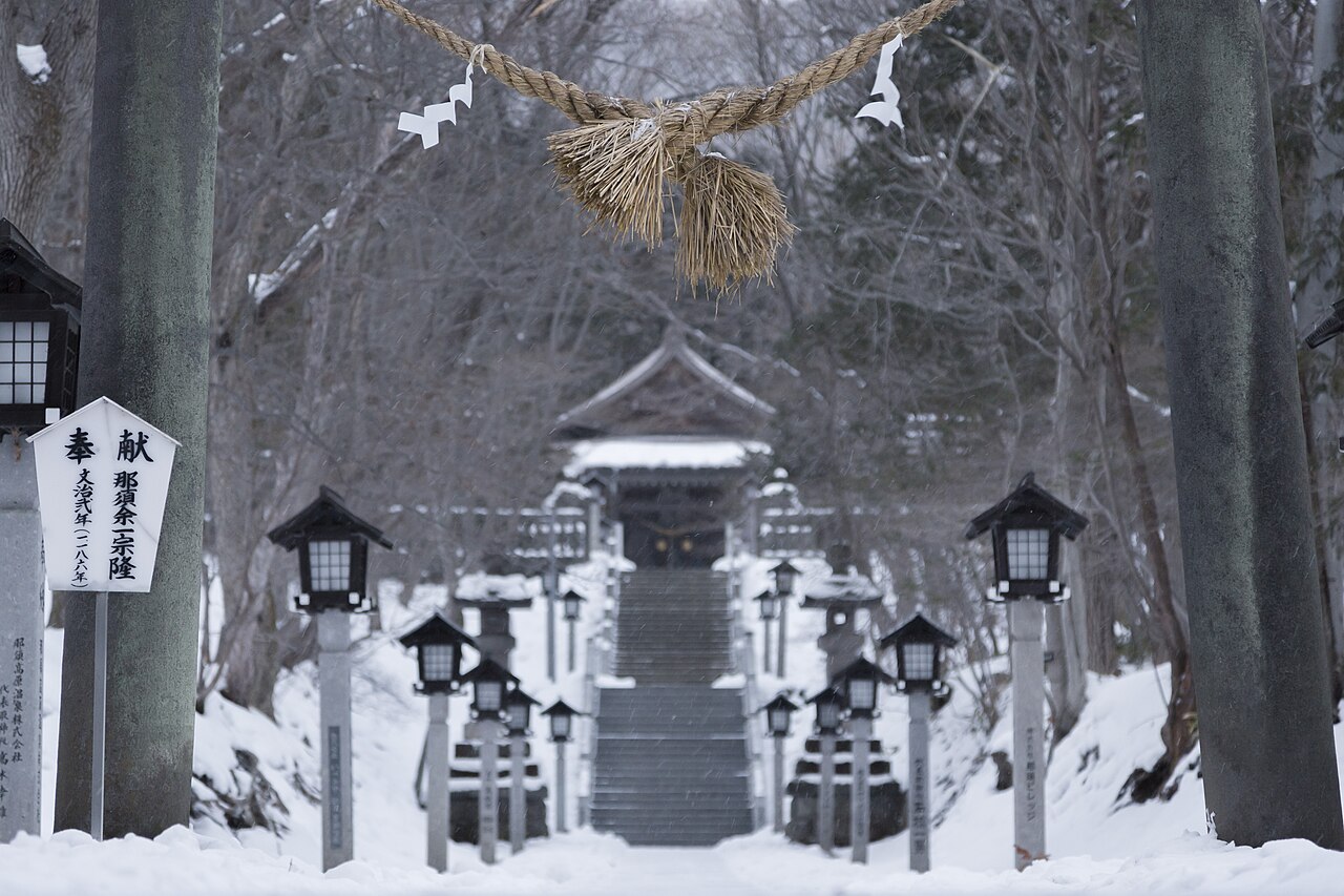 雪の那須温泉神社。しめ縄の下に灯籠が並ぶ参道と社殿