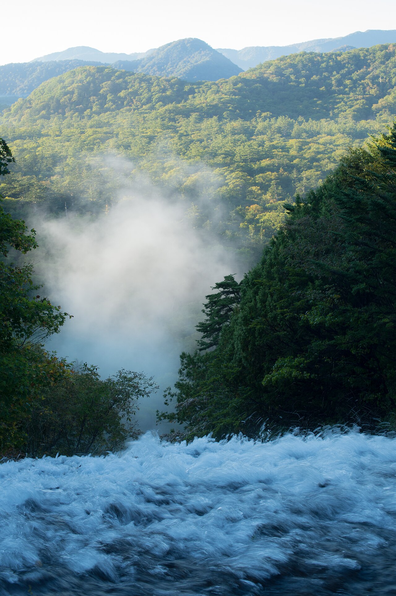 早朝の湯滝上部。立ちのぼる水煙と朝日に照らされた奥日光の山並み