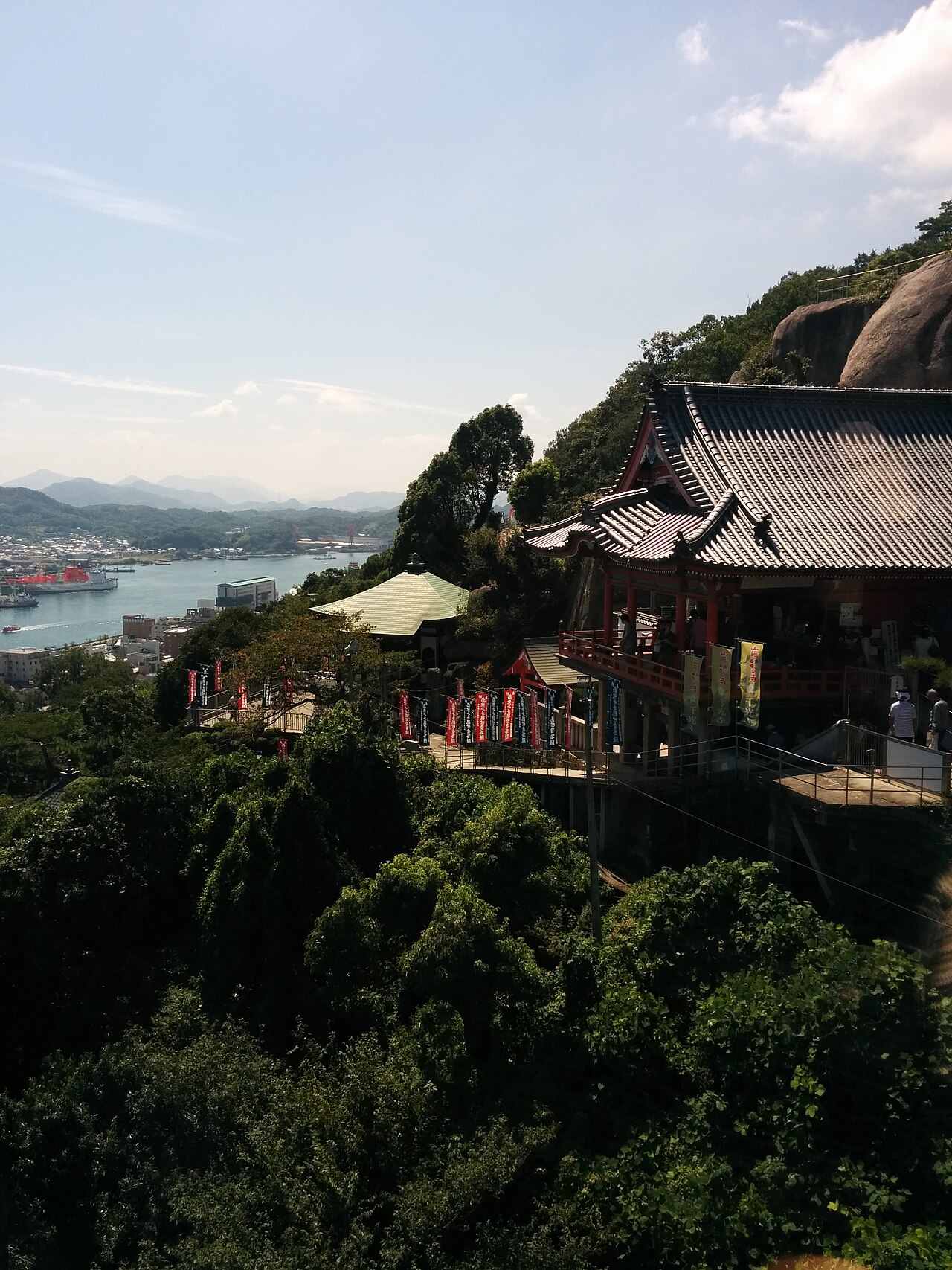 千光寺の本堂を岩と緑越しに見上げる