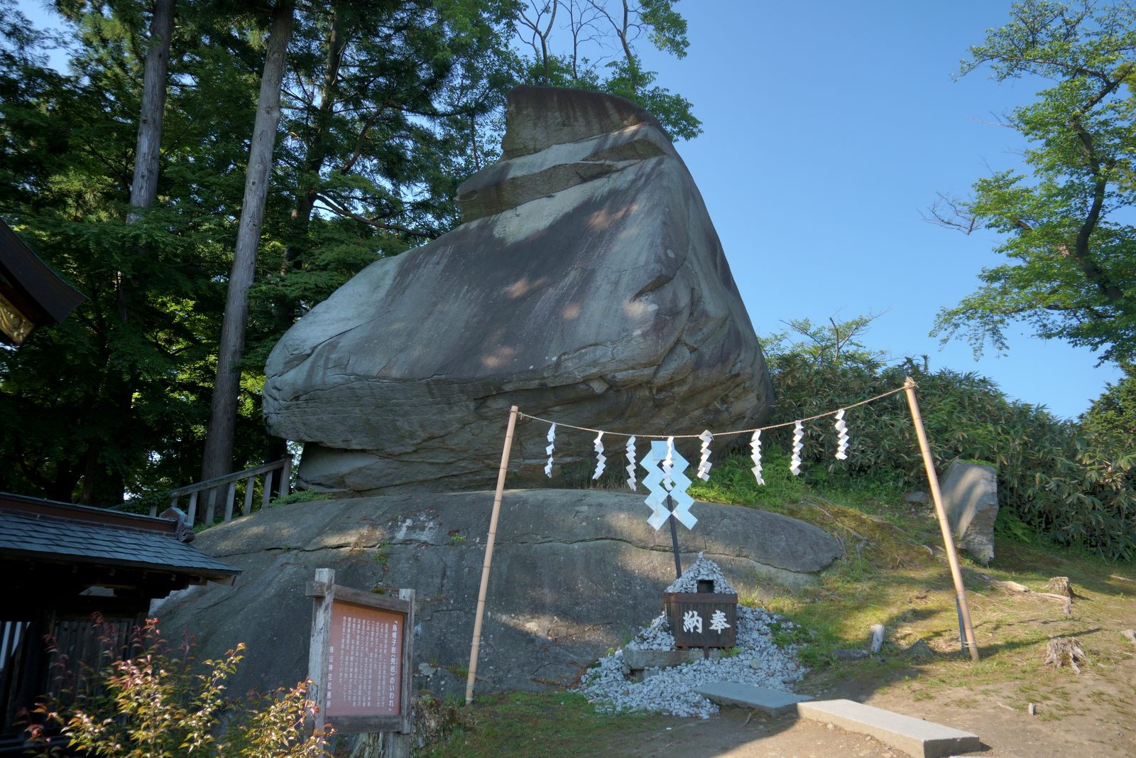 注連縄が張られた烏帽子岩の全景と由来を記した案内板