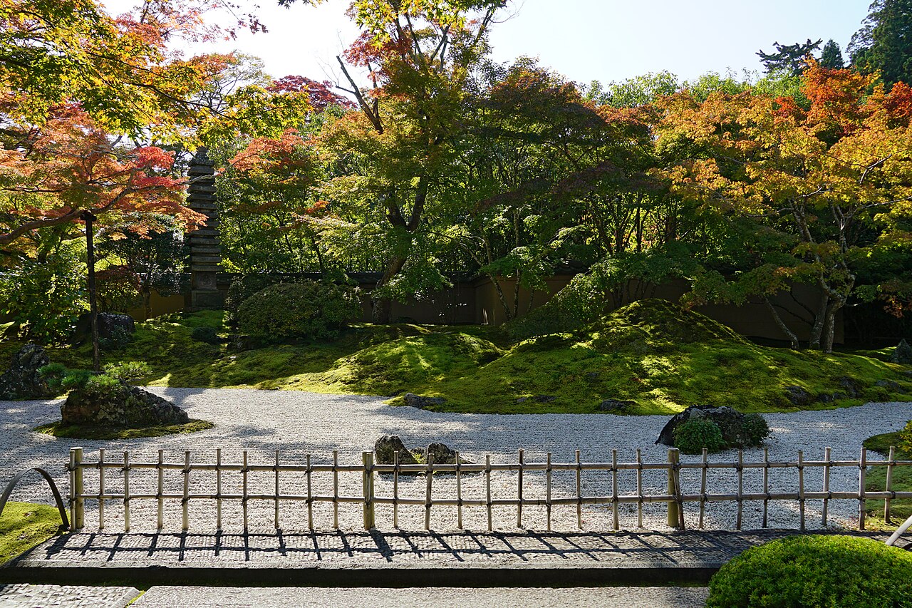 竹垣越しに見る苔の庭園と紅葉、五重塔状の石塔
