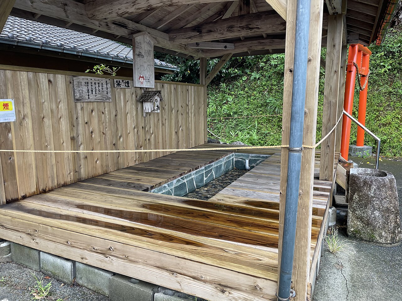 木造東屋の下の細長い石張りの湯、禁煙札と注意書き