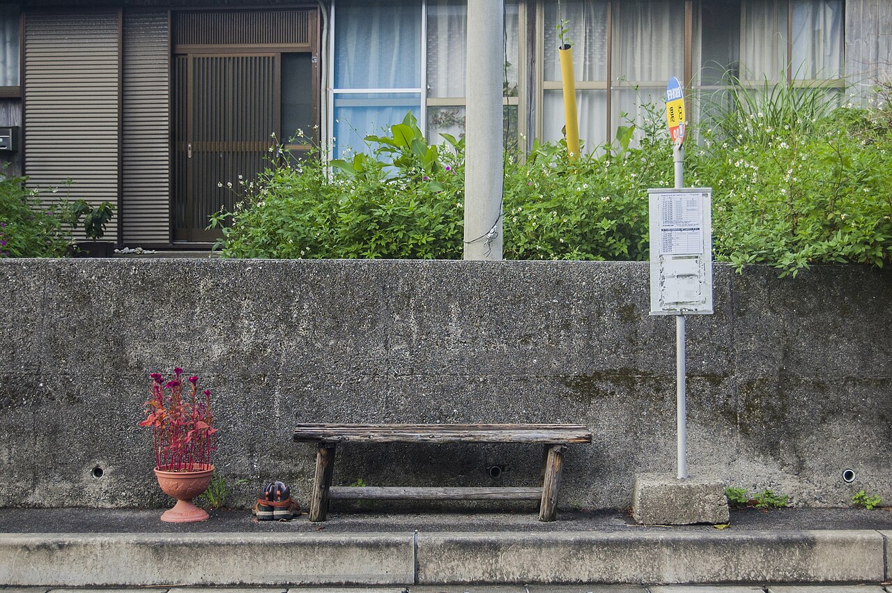 湯泊集落のバス停。木のベンチと時刻表の掲示板、鉢植えの花