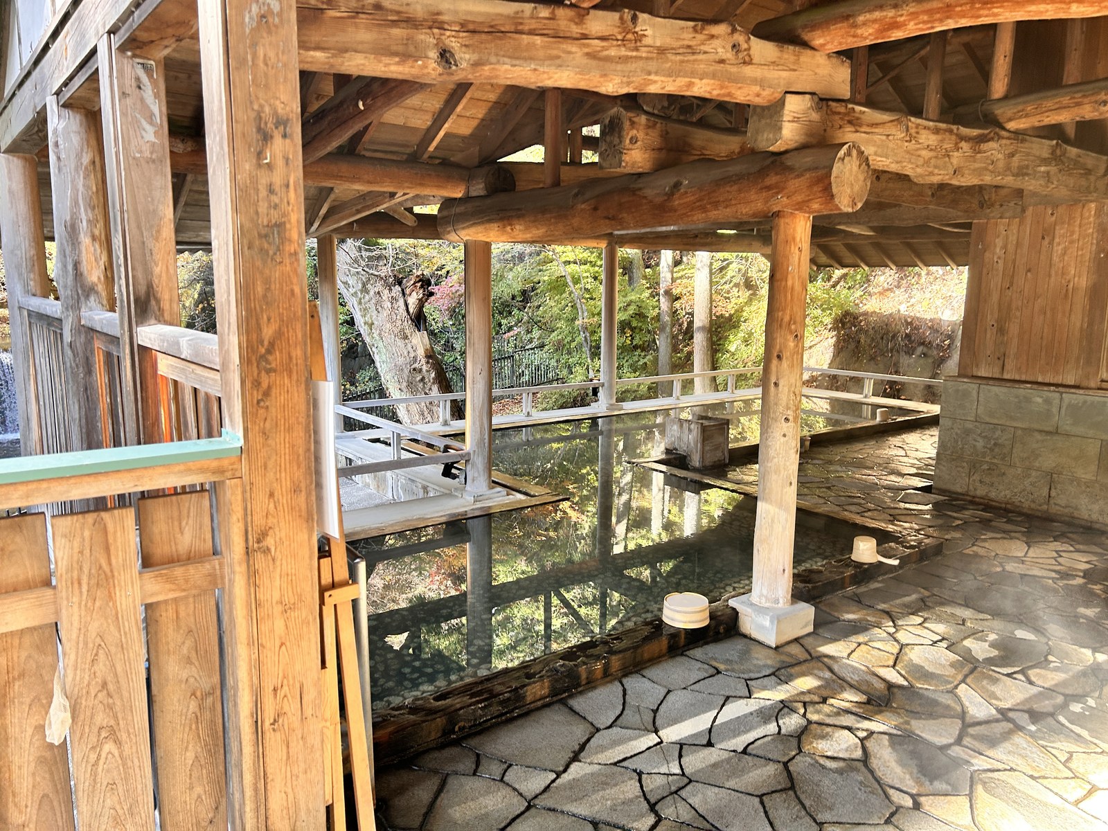 木造の梁が組まれた屋根の下、石畳に囲まれた四角い湯船に朝の光が差し込む四万温泉の湯