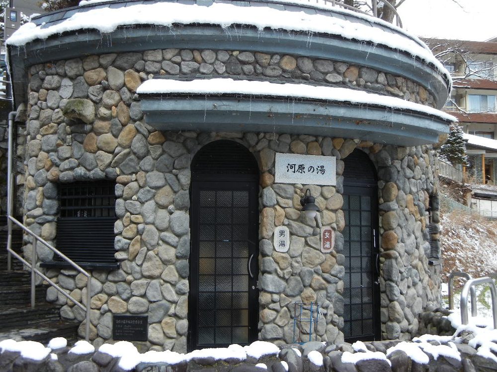 石造りの円形の建物に「河原の湯」の看板がかかる共同浴場