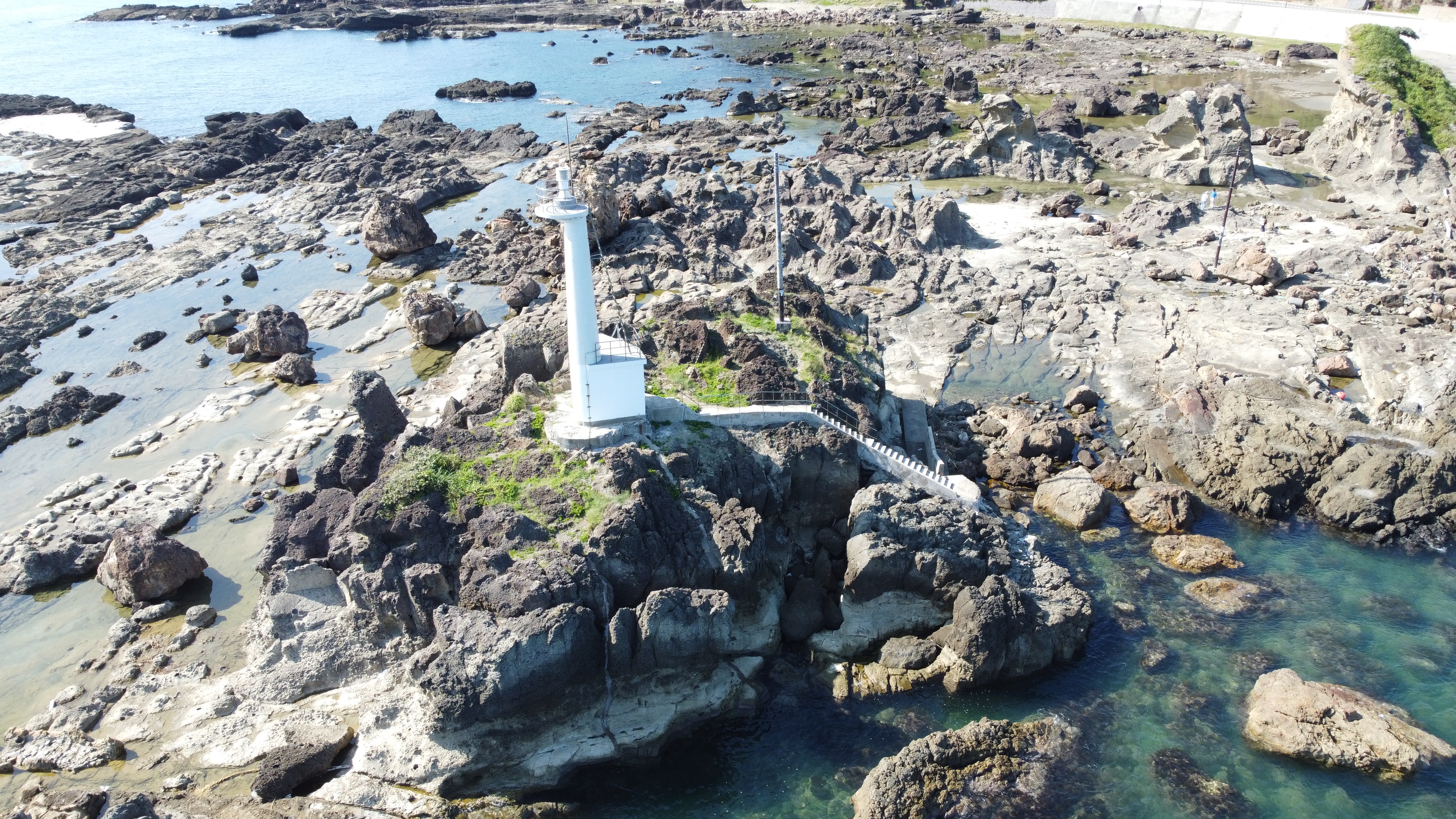 潮瀬崎の岩場と、カメ岩の上に立つ潮瀬埼灯台の空撮