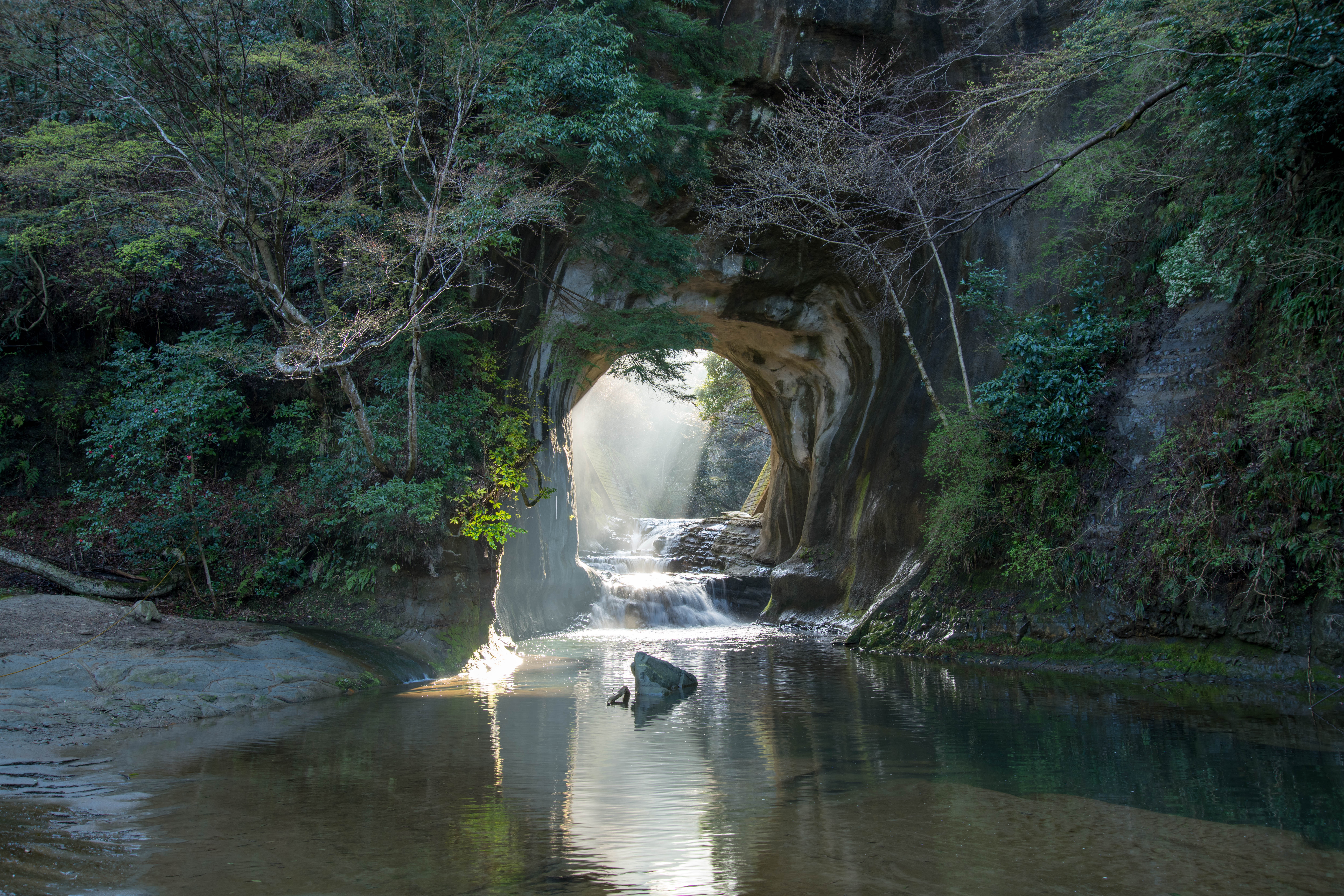 亀岩の洞窟に朝日が差し込み、光の筋が水面を照らす様子